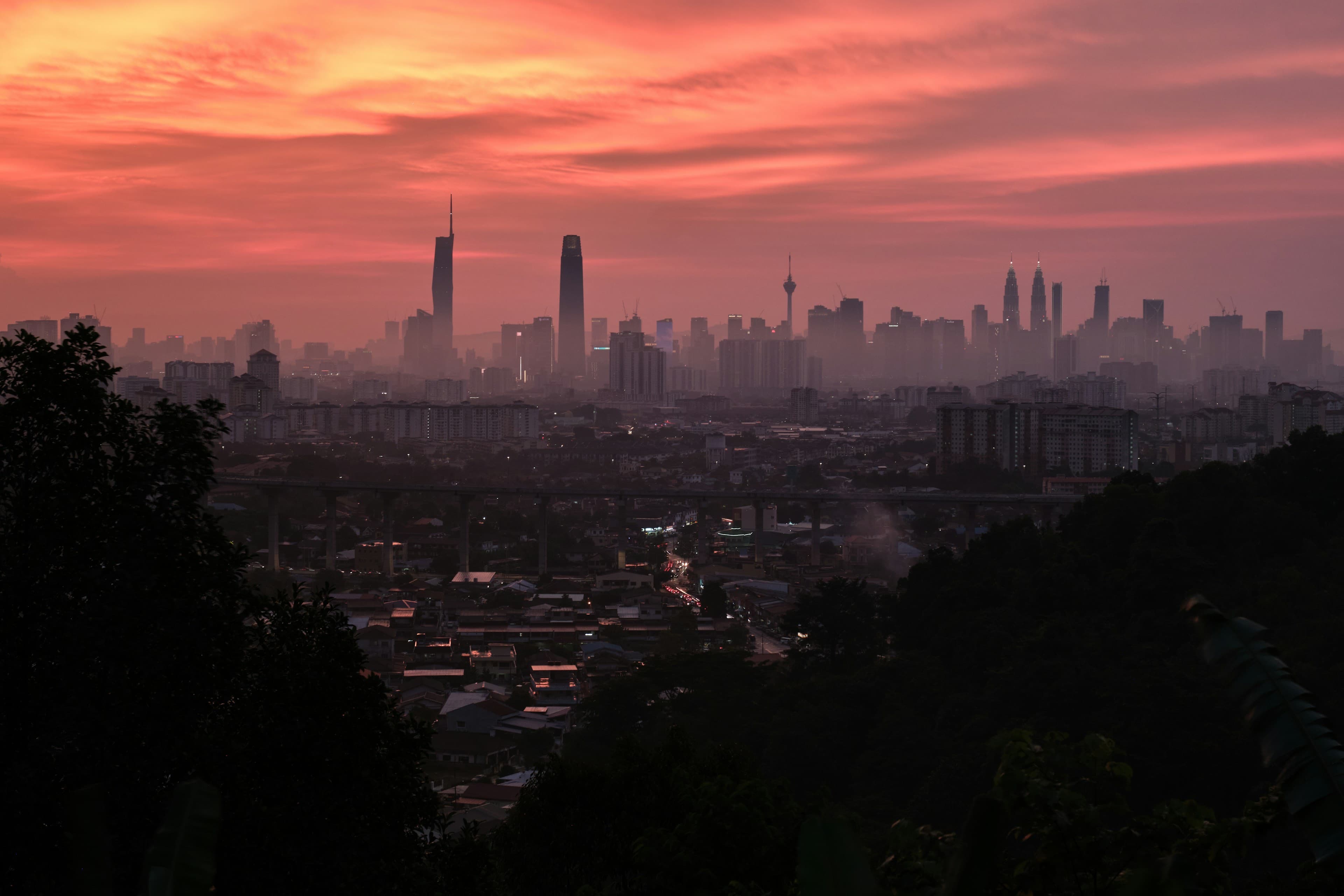 The Kuala Lumpur skyline at fiery sunset — the Petronas Twin Towers, KL Tower and Merdeka 118 silhouetted against a red sky.