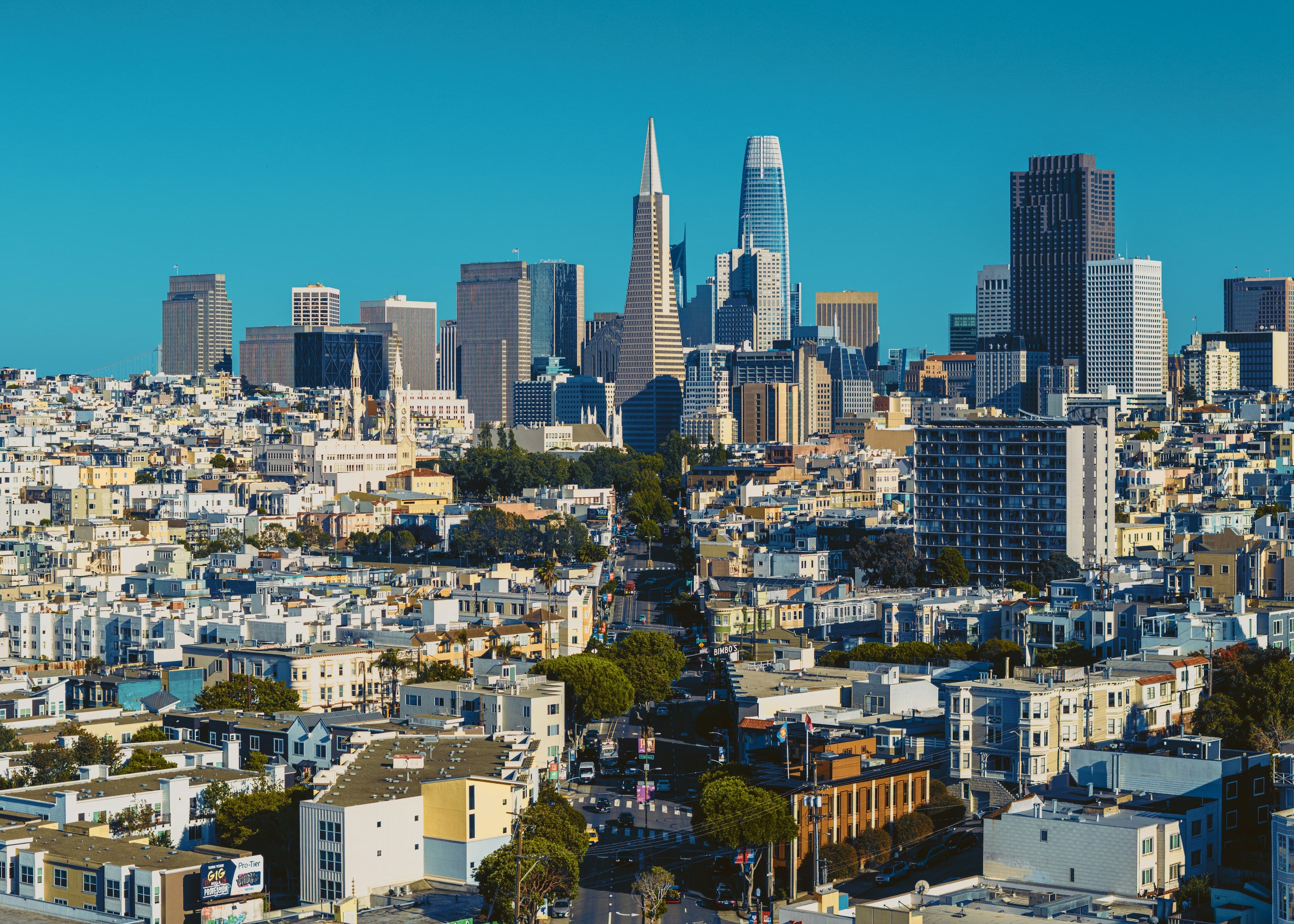 A view over San Francisco's rooftops to the downtown skyline, the Transamerica Pyramid and Salesforce Tower against a deep blue sky.