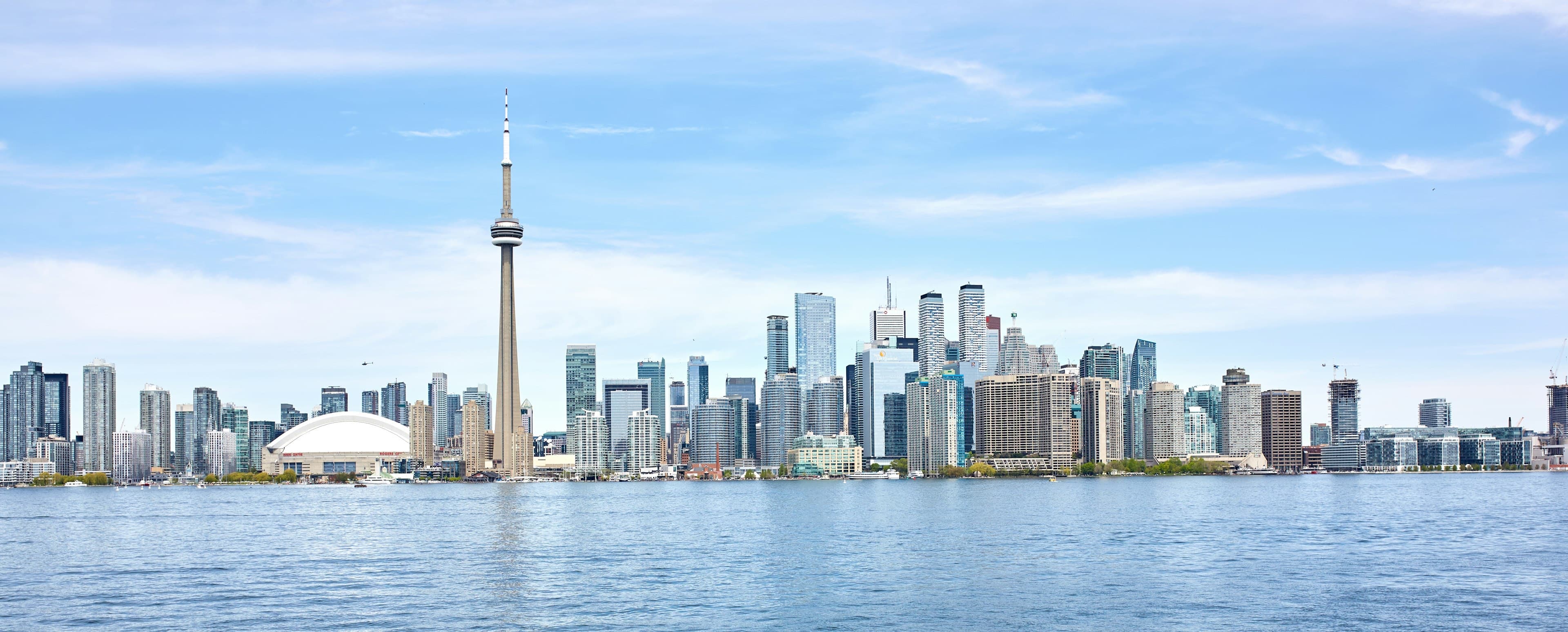 The Toronto skyline across Lake Ontario on a clear day, the CN Tower rising above the downtown towers.