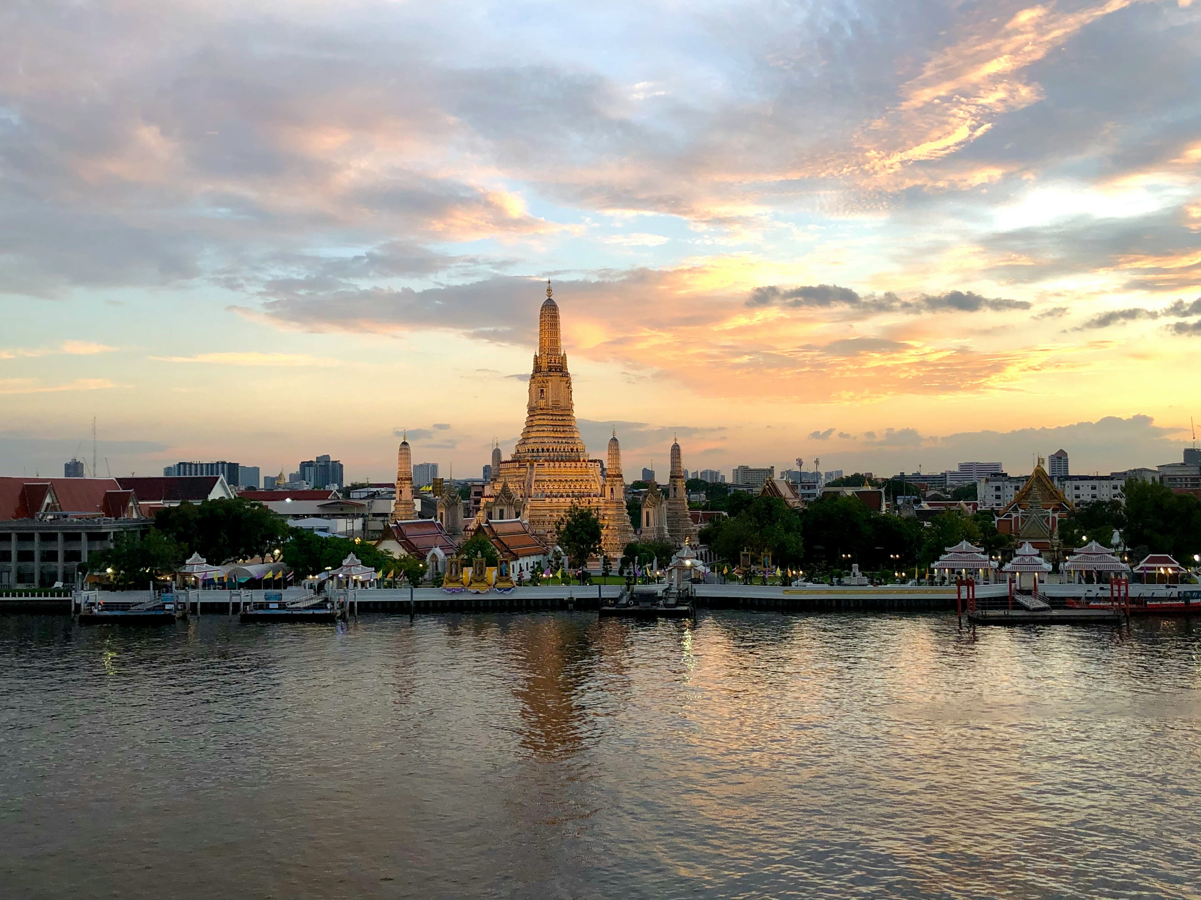 Wat Arun, the Temple of Dawn, lit gold across the Chao Phraya river in Bangkok at sunset.
