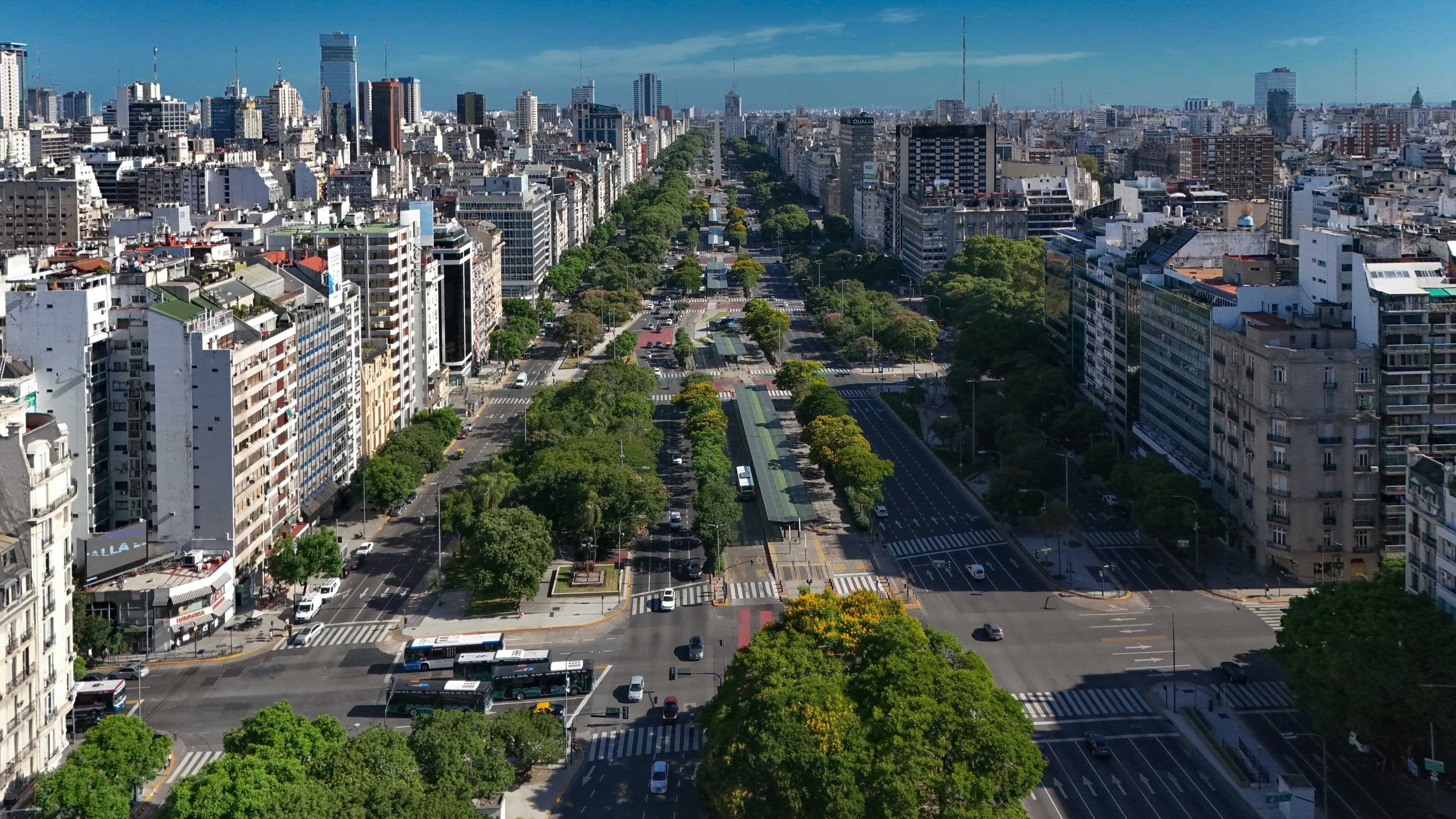 Aerial view down Avenida 9 de Julio in Buenos Aires, the tree-lined avenue and the Obelisco stretching into the city skyline.