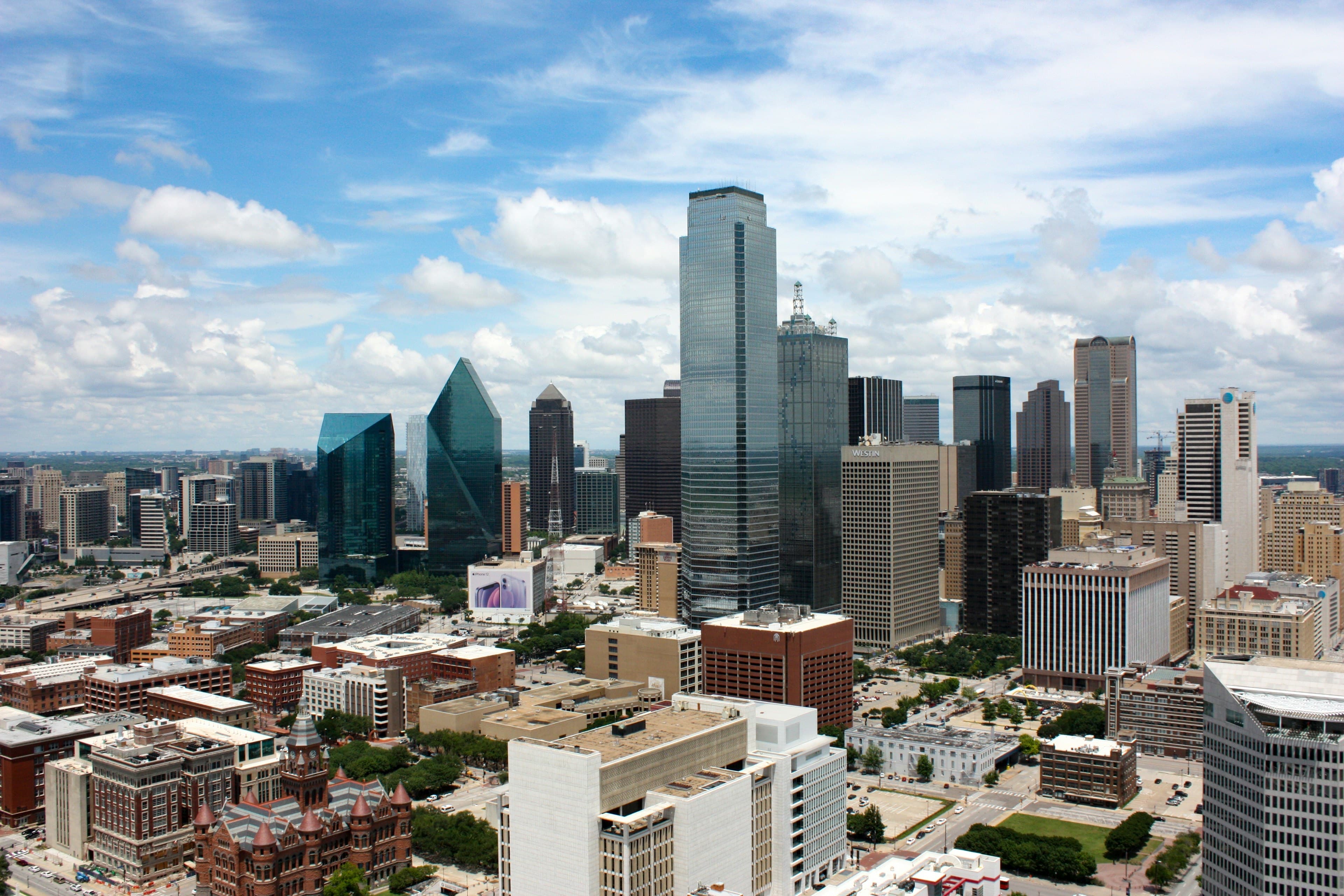 The downtown Dallas skyline under a bright blue sky, the green glass prism of Fountain Place among the towers.