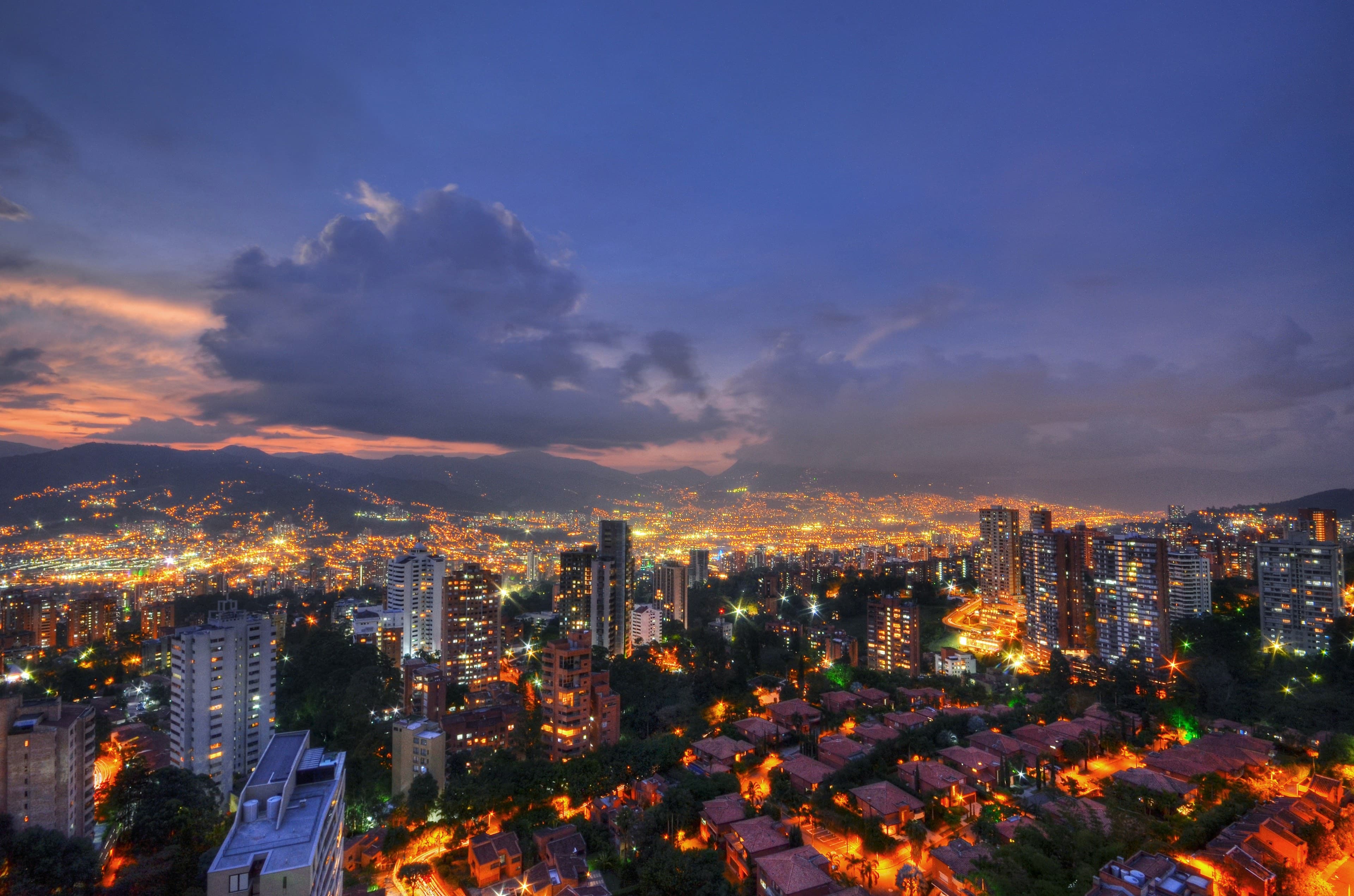 The El Poblado skyline of Medellín at dusk, city lights filling the Aburrá Valley with the Andes and a pink sunset behind.