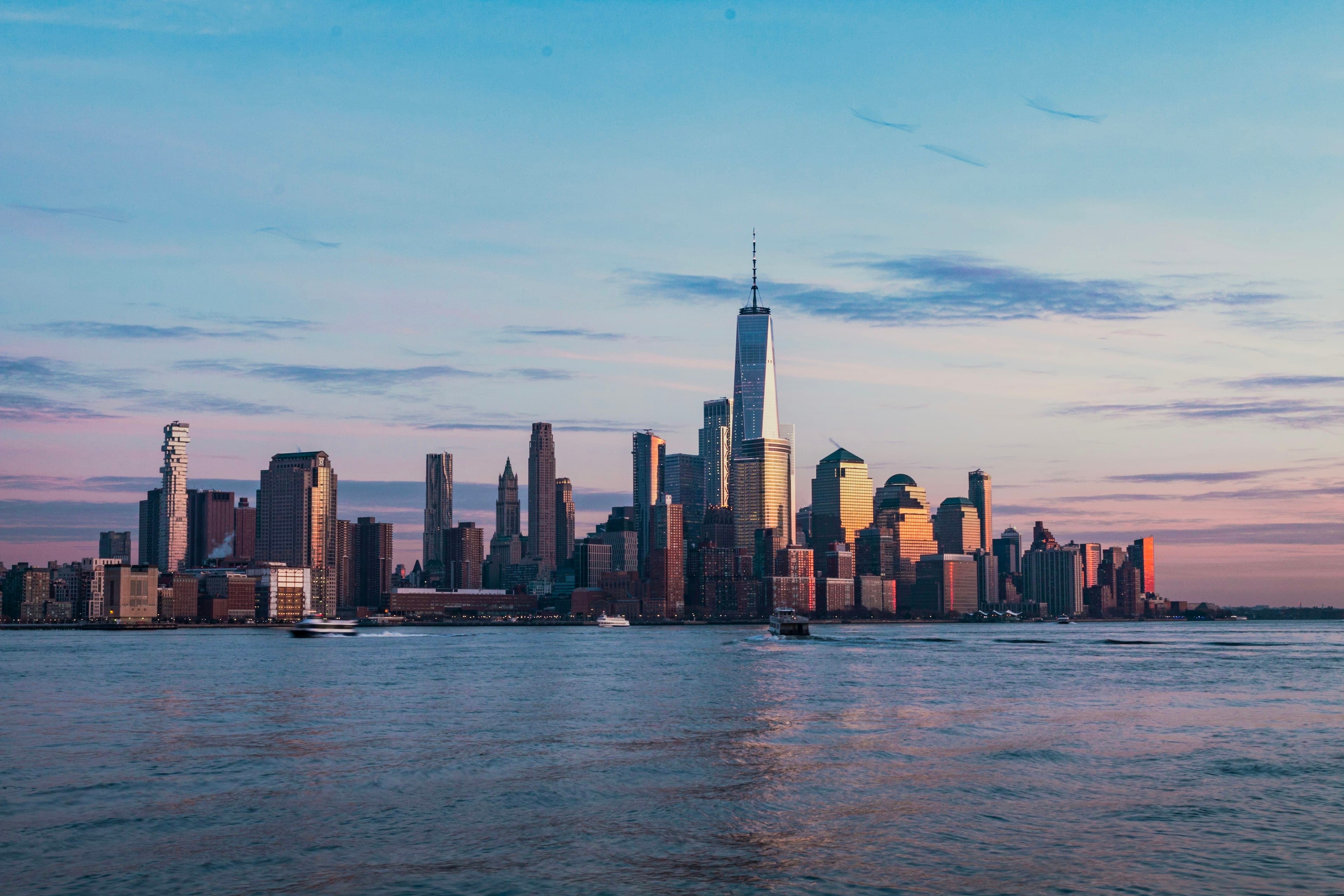 The Lower Manhattan skyline across the Hudson at golden hour, One World Trade Center rising above the Financial District.