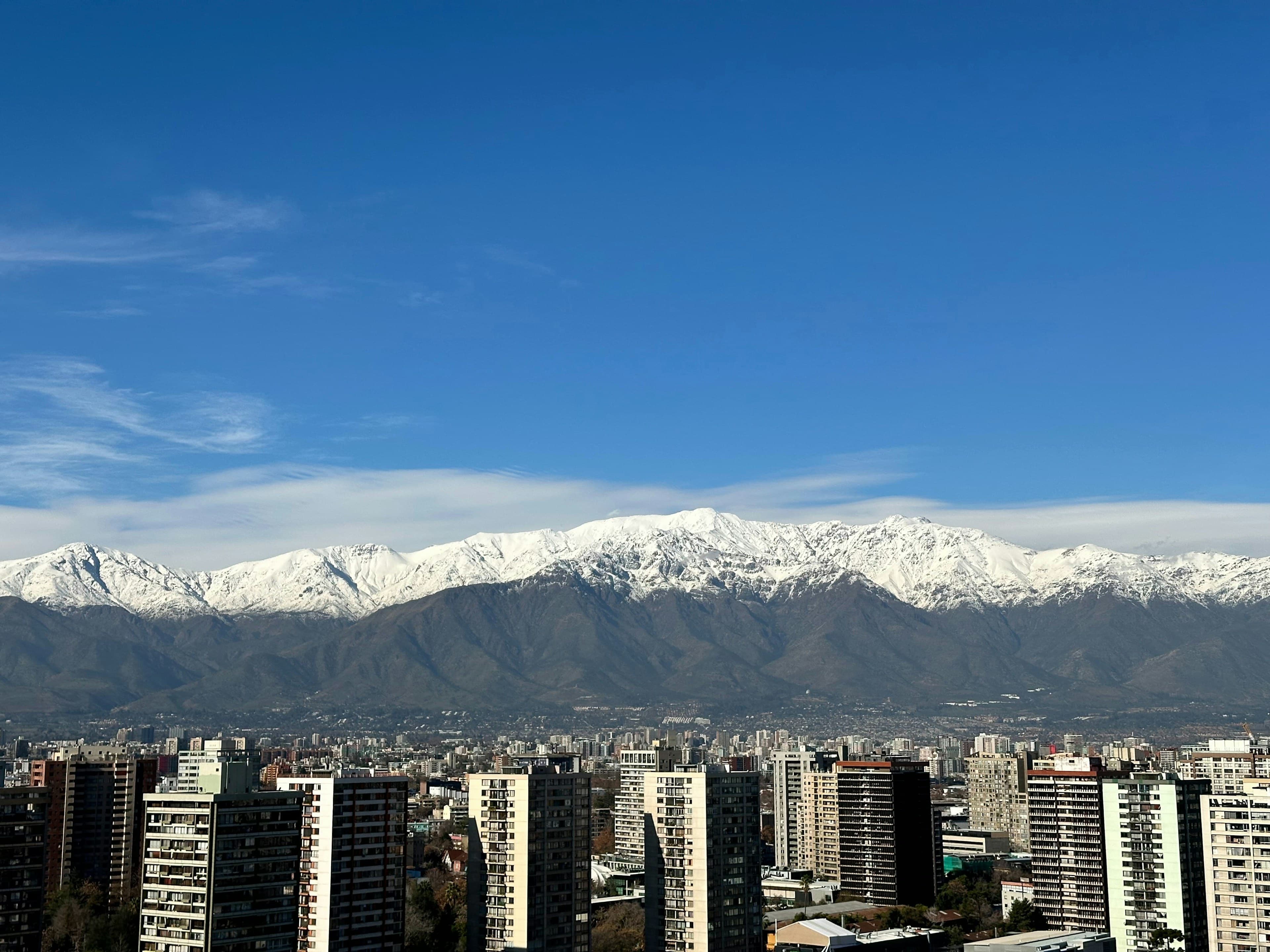 Santiago's high-rises below the snow-capped Andes, the white peaks filling the frame under a deep blue sky.