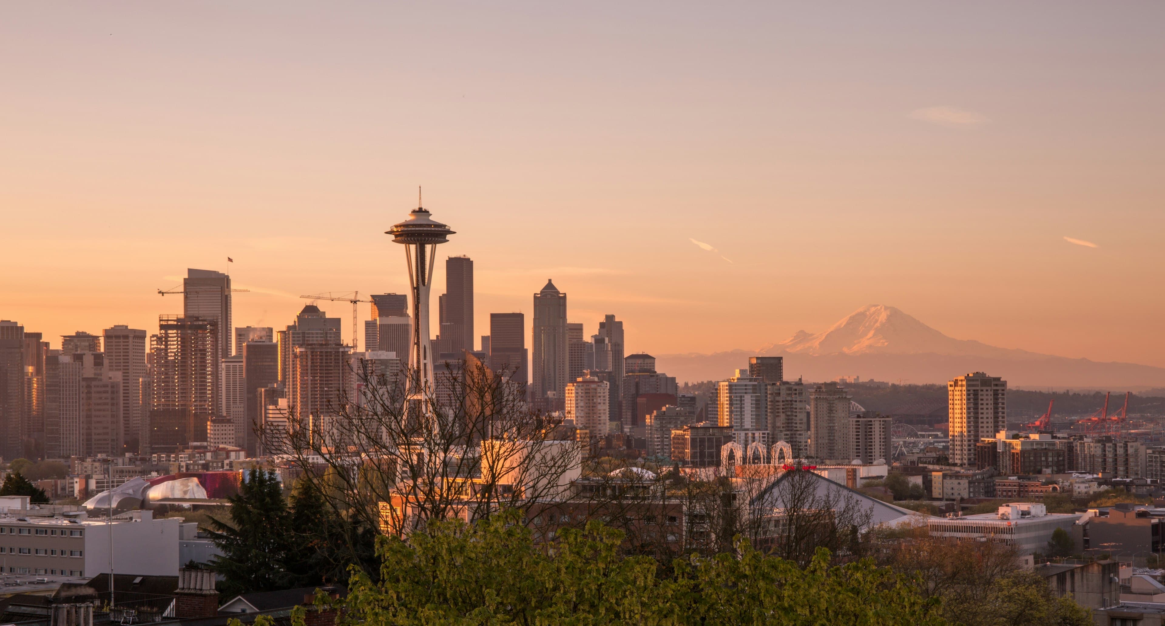 The Space Needle and downtown Seattle skyline at sunset with Mount Rainier glowing on the horizon.