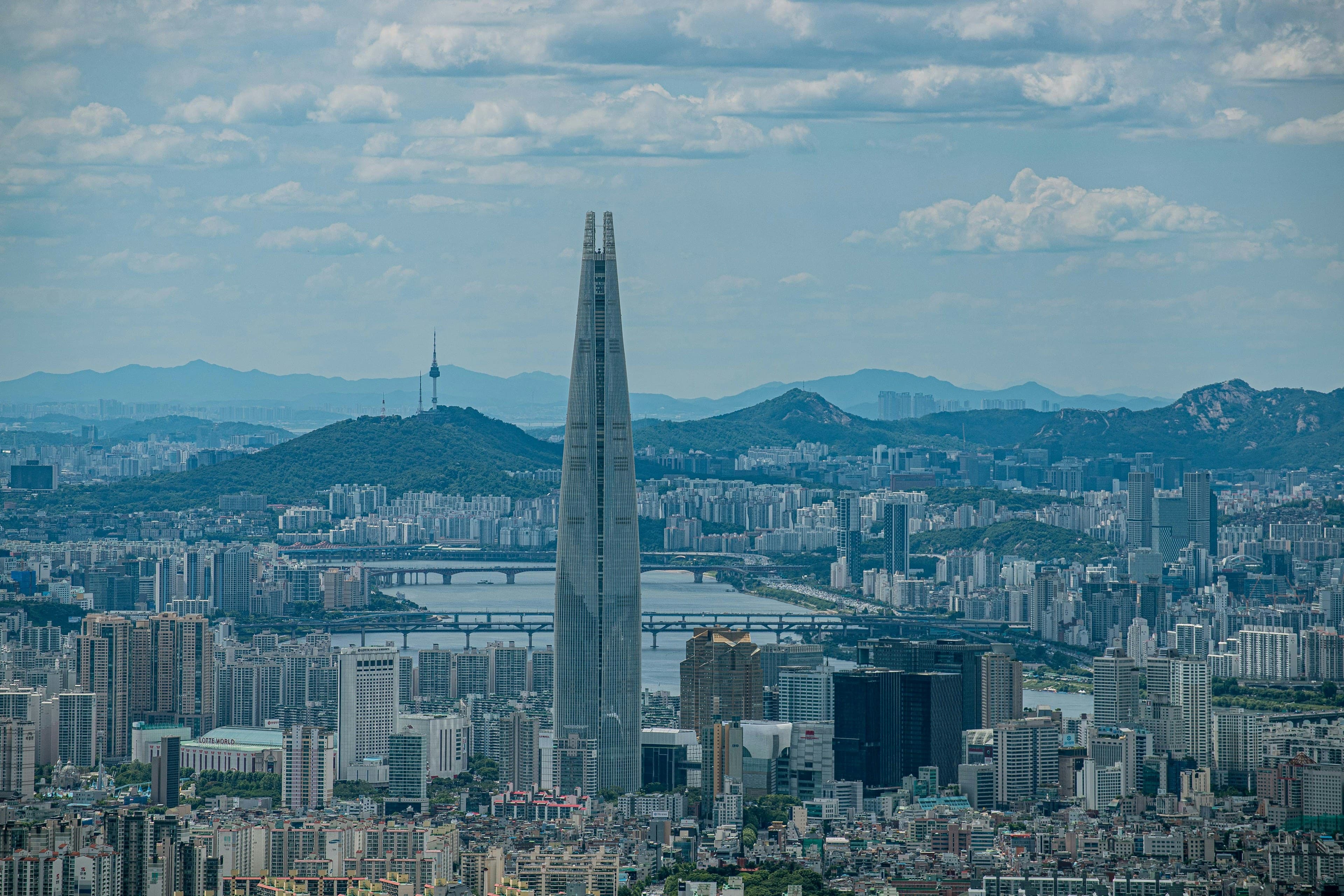 The Lotte World Tower rising over Seoul and the Han river, with N Seoul Tower on Namsan and the mountains ringing the city.