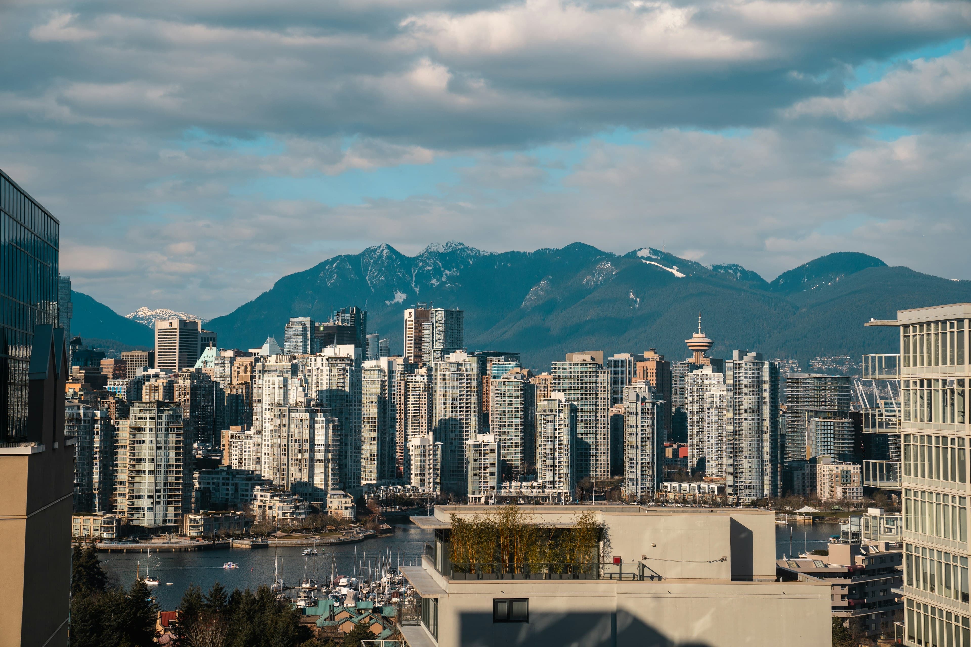 The downtown Vancouver skyline against the snow-capped North Shore mountains, boats moored in the harbor below.